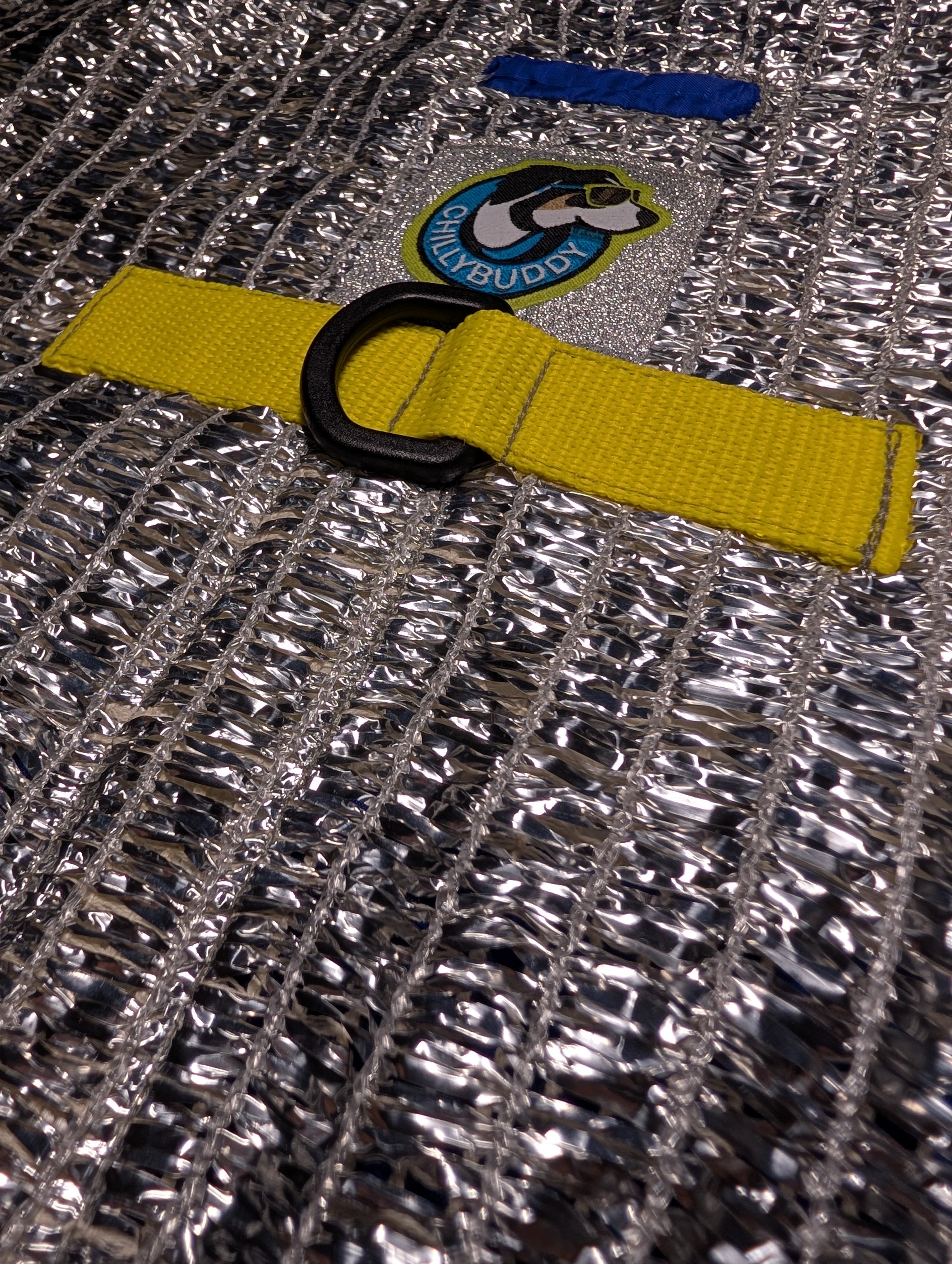 Close-up of a silver reflective mesh fabric with a bright yellow webbing strap and a black D-ring for hardness.