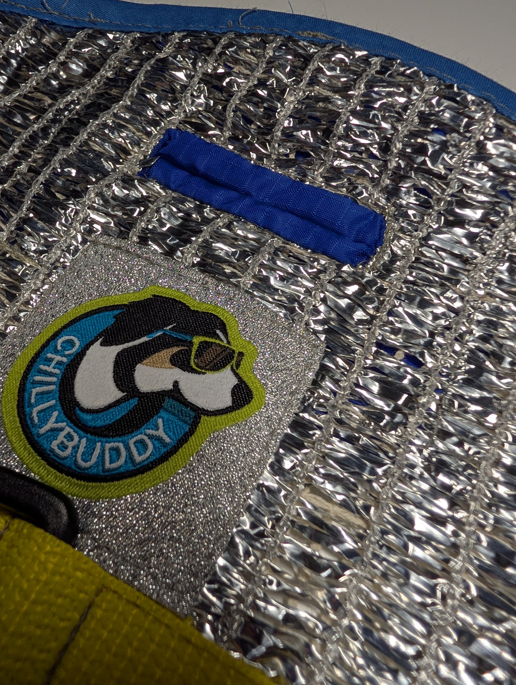 Close-up of a blue-stitched leash hole built into a silver reflective insulated material, and a circular 'Chillybuddy' dog patch.