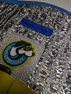 Close-up of a blue-stitched leash hole built into a silver reflective insulated material, and a circular 'Chillybuddy' dog patch.
