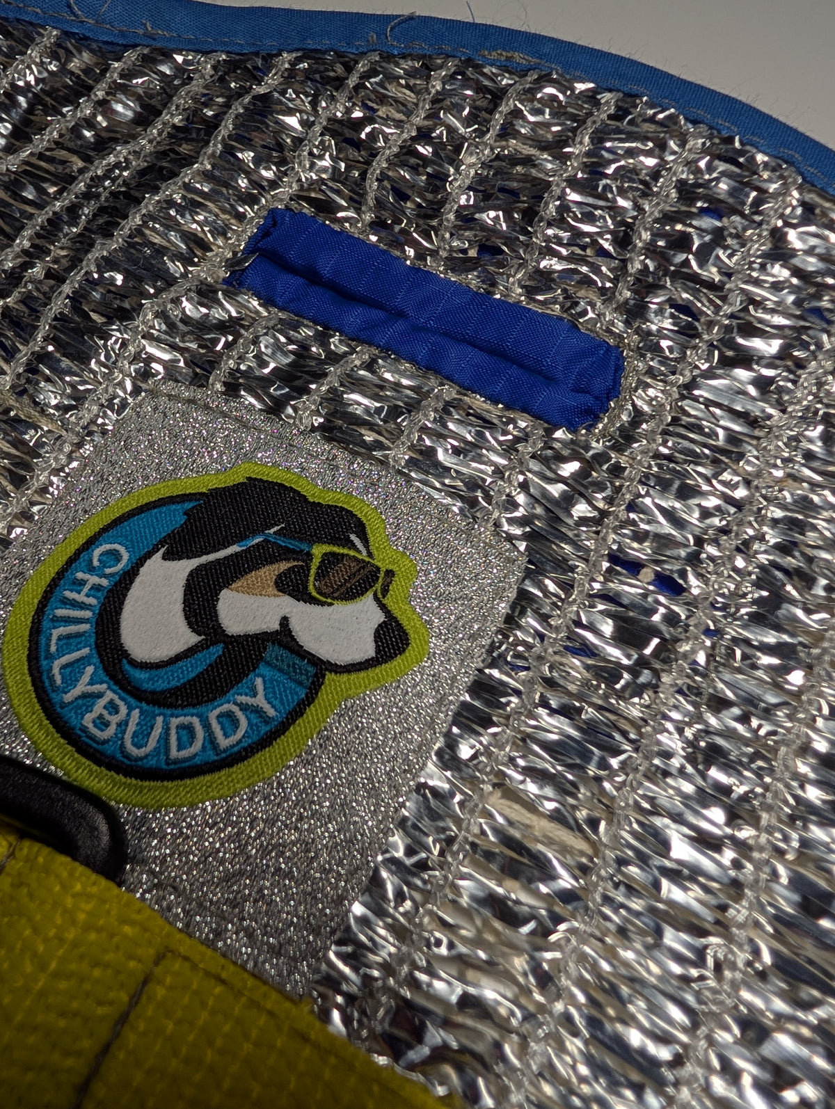 Close-up of a blue-stitched leash hole built into a silver reflective insulated material, and a circular 'Chillybuddy' dog patch.